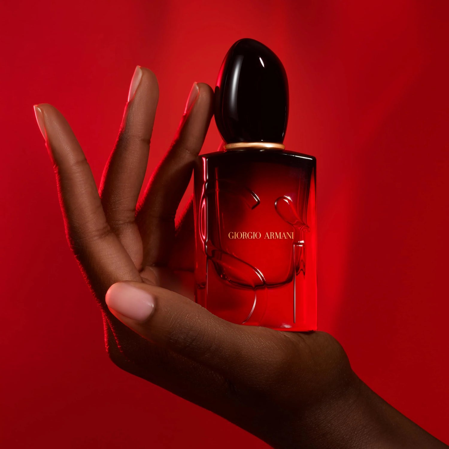 Hand holding a red Giorgio Armani perfume bottle against a red background