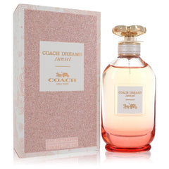 Coach Dreams Sunset Eau de Parfum bottle with a gold cap next to its pink glitter-patterned packaging box on a white background.