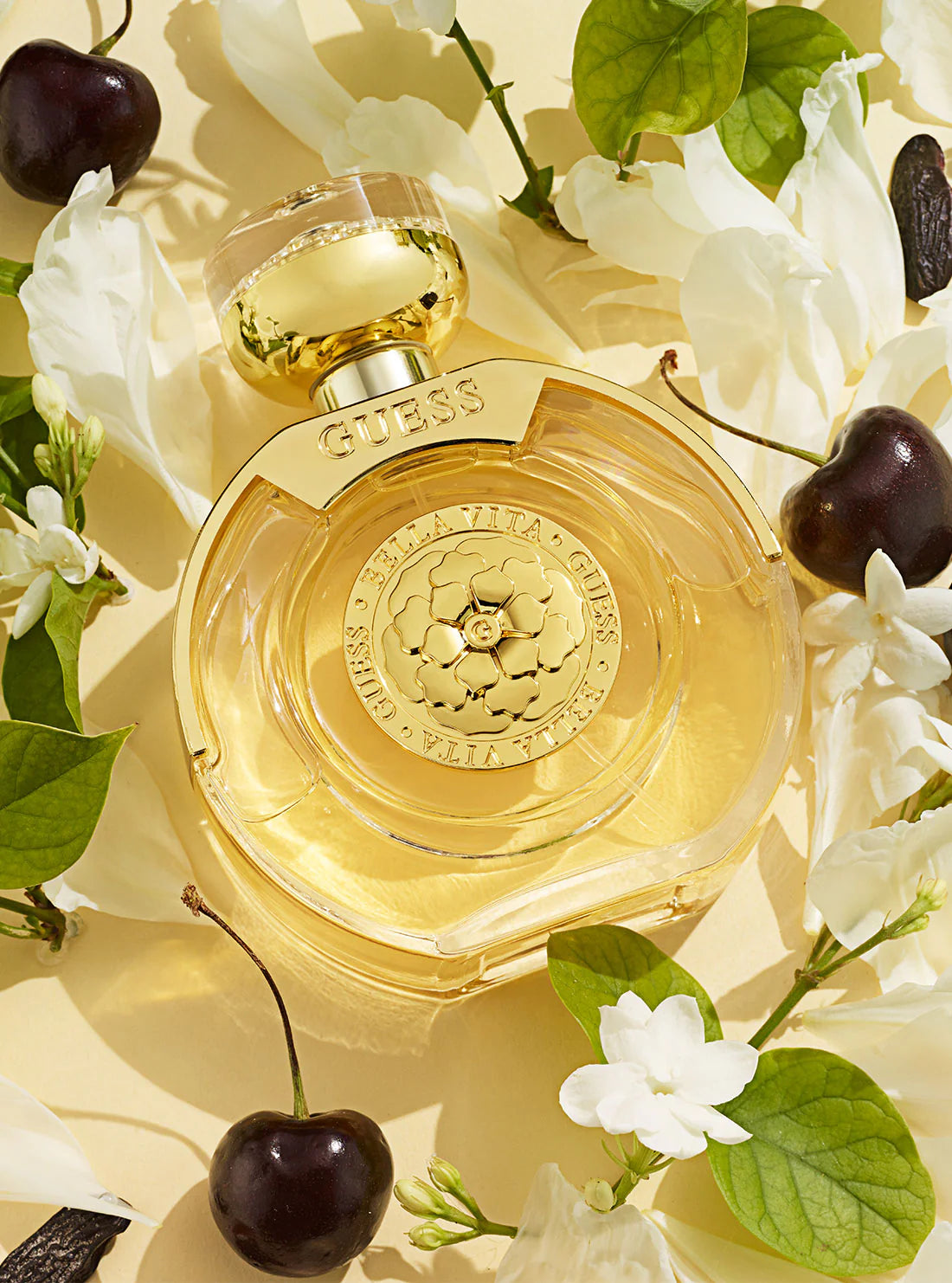 Guess perfume bottle surrounded by flowers and cherries on a light background