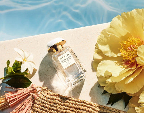Perfume bottle with flowers and a woven bag by a poolside