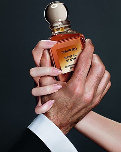 Hand holding a Tom Ford Santal Blush perfume bottle against a dark background