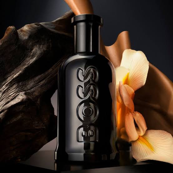 Black bottle with intricate design on a dark background with flowers