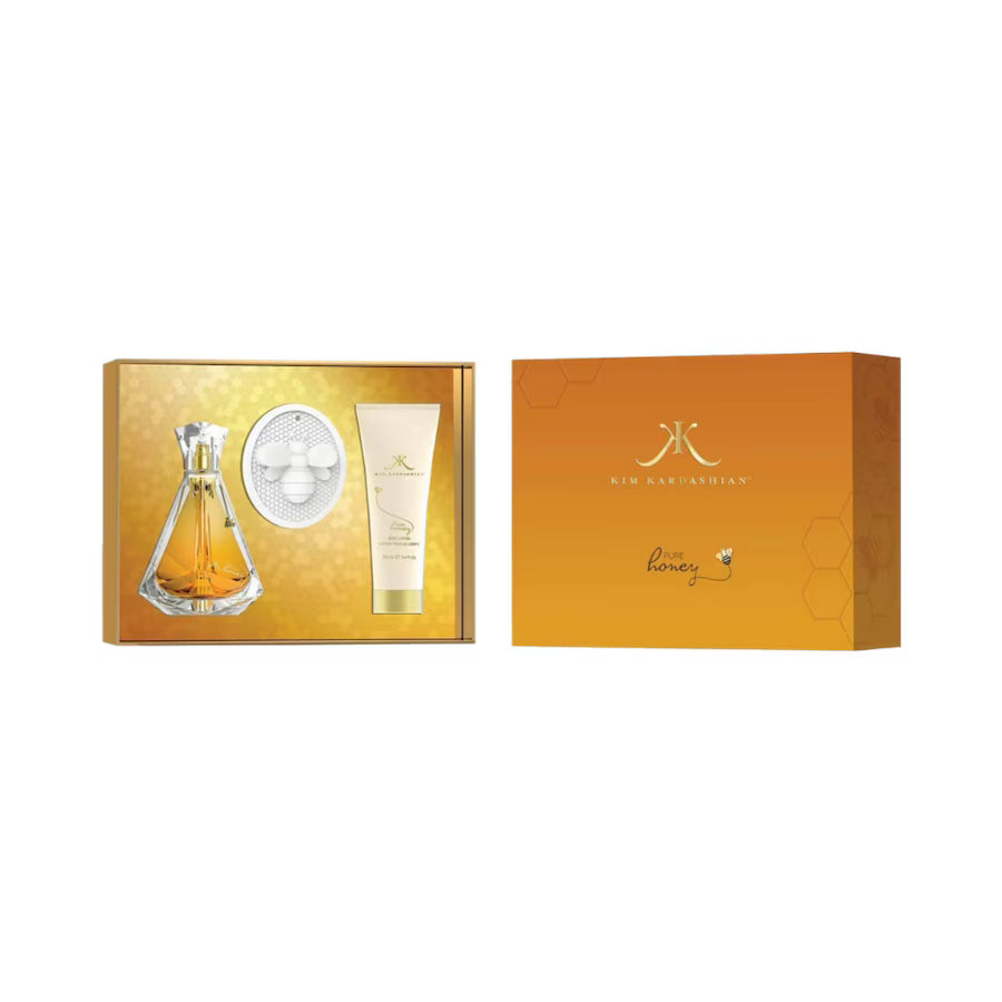 A perfume gift set displayed on a white background, featuring an open gold box with a clear glass perfume bottle, a round white diffuser, and a cream-colored body care tube, alongside a closed orange-gold outer box with a gold logo.
