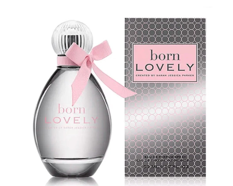 A bottle of Sarah Jessica Parker's 'born LOVELY' perfume next to its packaging box. The perfume bottle is clear glass with a silver-toned base and cap, decorated with a light pink ribbon tied in a bow around the neck.